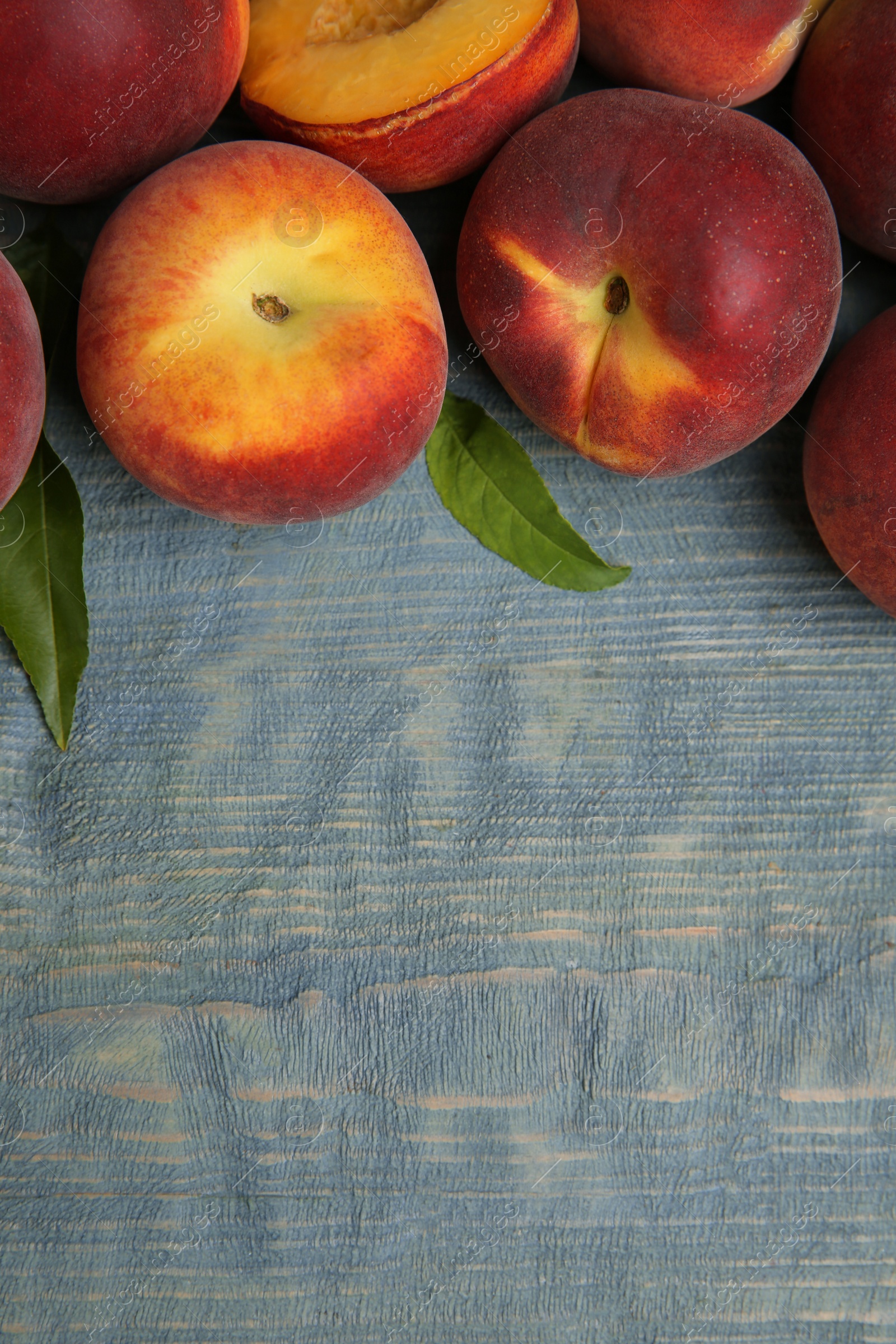 Photo of Fresh peaches and leaves on blue wooden table, top view with space for text