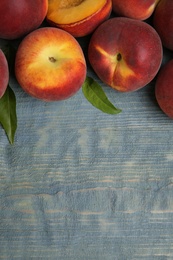 Photo of Fresh peaches and leaves on blue wooden table, top view with space for text