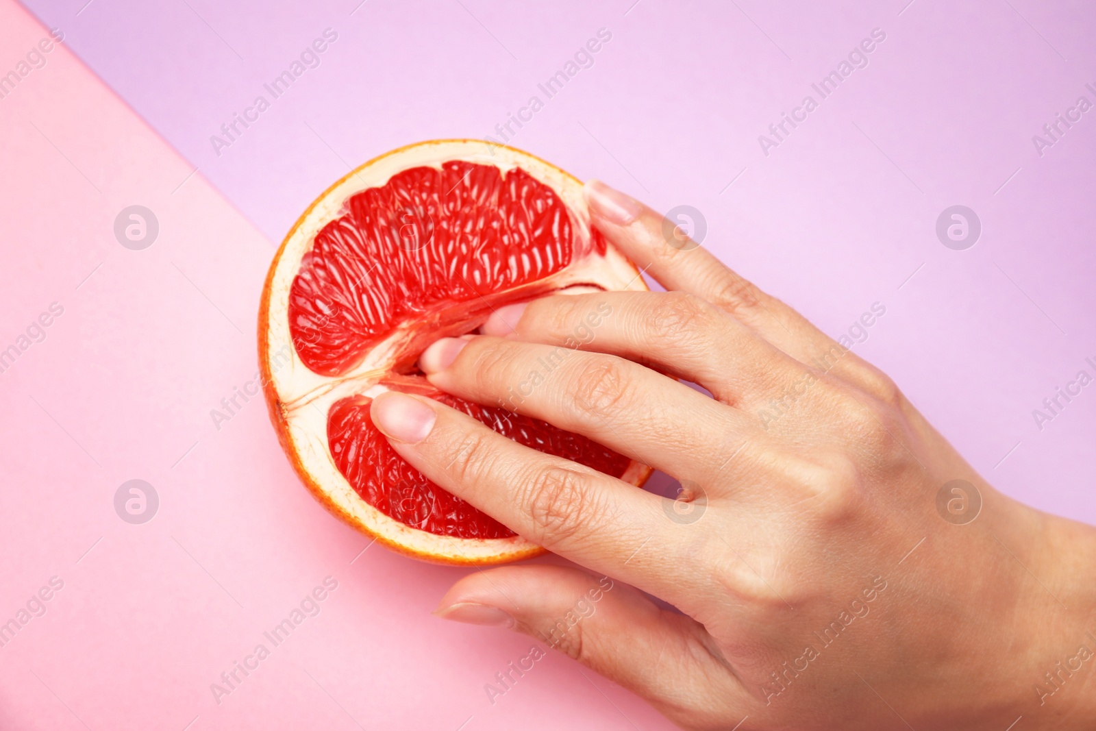 Photo of Young woman touching half of grapefruit on color background, above view. Sex concept