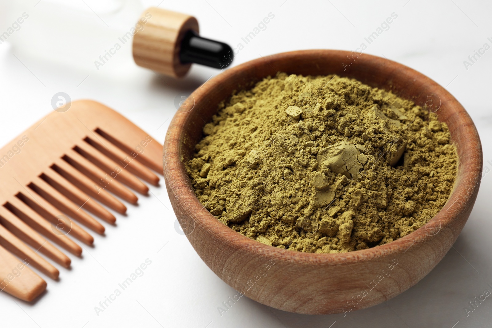 Photo of Bowl of henna powder, pipette and comb on white marble table