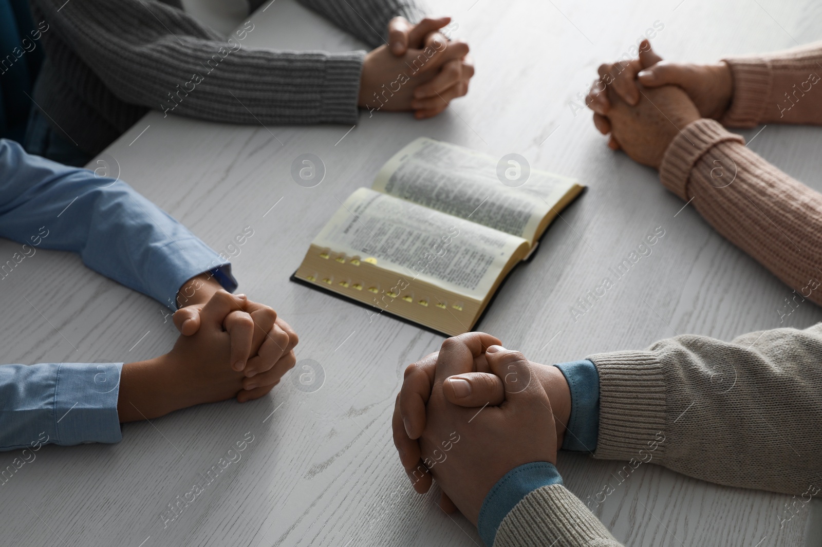Photo of Boy and his godparents praying together at white wooden table, closeup