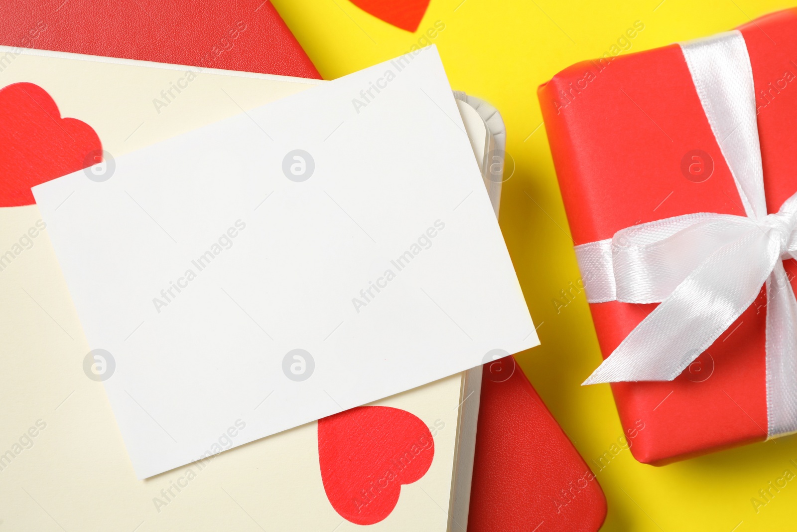 Photo of Blank card, gift box and notebooks on yellow background, flat lay with space for text. Valentine's Day celebration