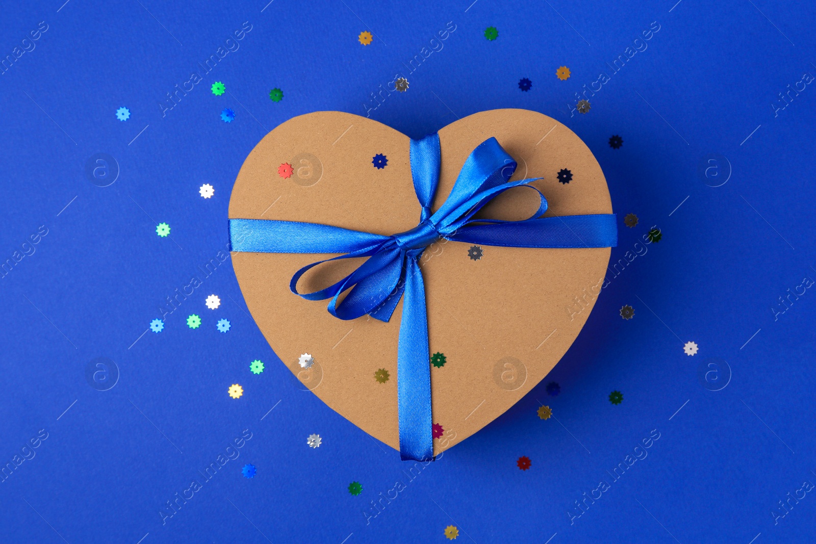 Photo of Beautiful heart shaped gift box with bow and confetti on blue background, top view