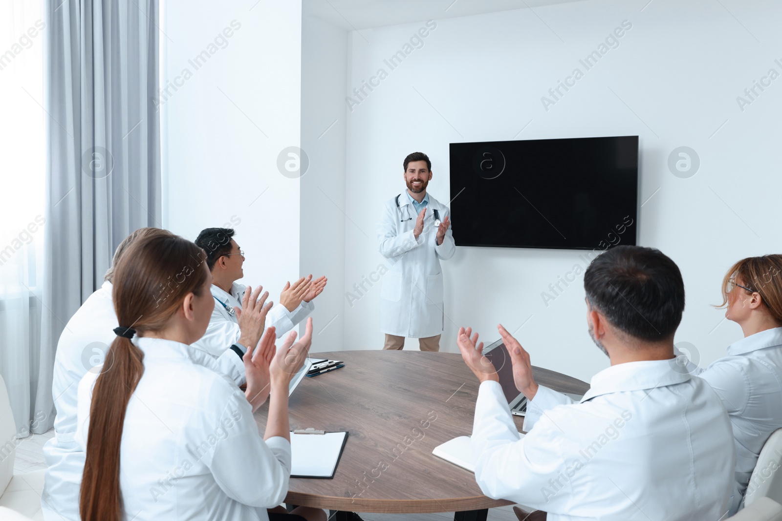 Photo of Team of doctors listening to speaker report near tv screen in meeting room. Medical conference