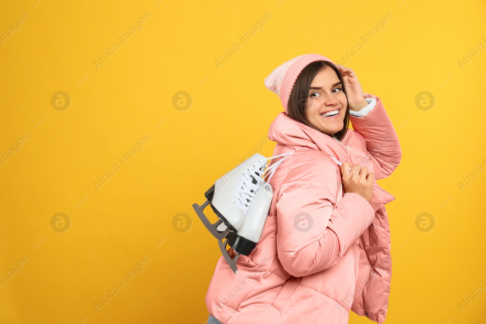 Photo of Happy woman with ice skates on yellow background. Space for text