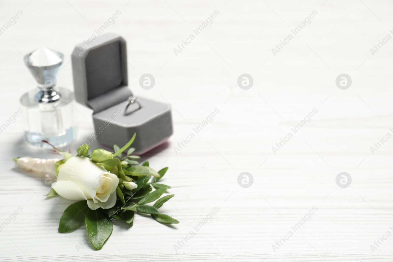 Photo of Wedding stuff. Stylish boutonniere, perfume and ring on white wooden table, closeup. Space for text