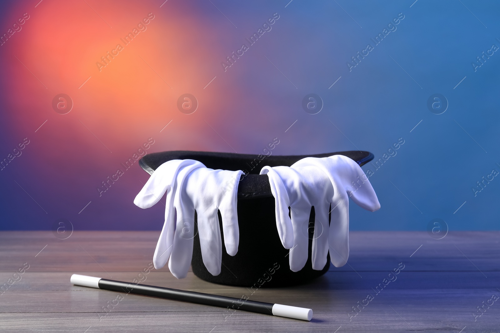 Photo of Magician's hat, wand and gloves on wooden table against color background