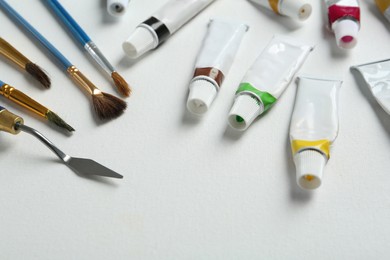 Photo of Brushes, spatula and paints on blank canvas, closeup