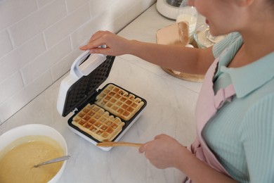 Woman making delicious Belgian waffles in kitchen, closeup