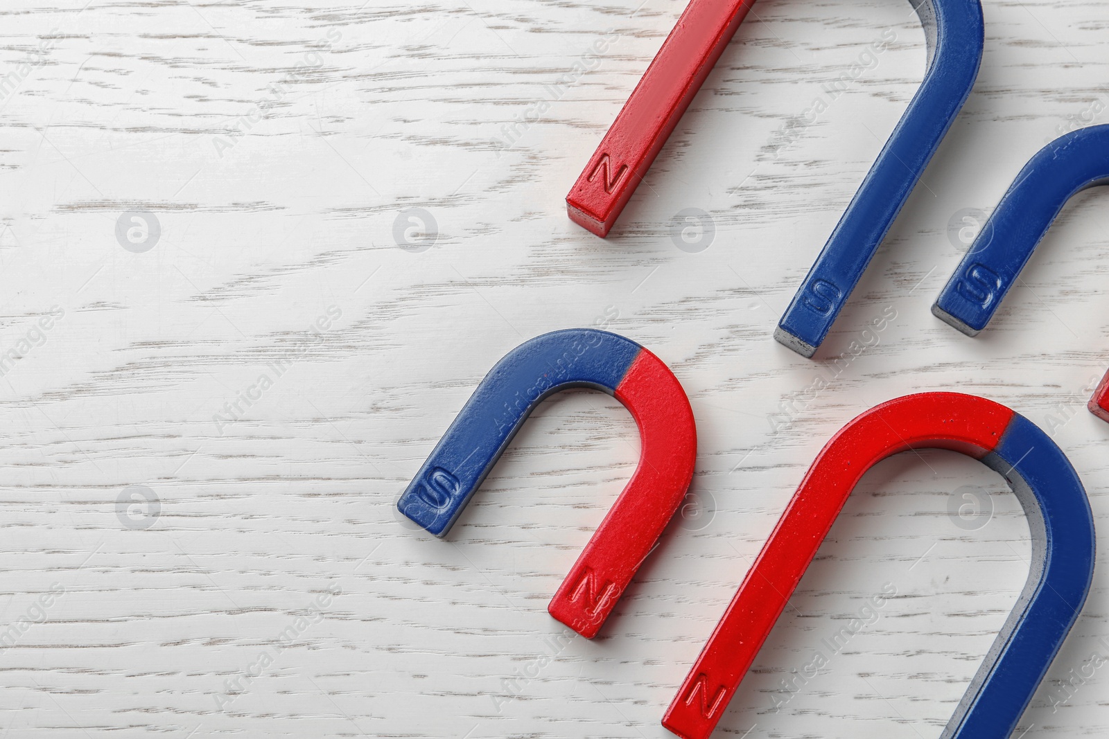 Photo of Red and blue horseshoe magnets on wooden background, top view with space for text