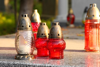 Photo of Different grave lanterns with burning candles on granite tombstone outdoors. Funeral ceremony