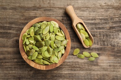 Photo of Bowl and scoop with peeled pumpkin seeds on wooden table, flat lay