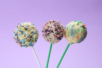 Delicious confectionery. Sweet cake pops decorated with sprinkles on light violet background, closeup