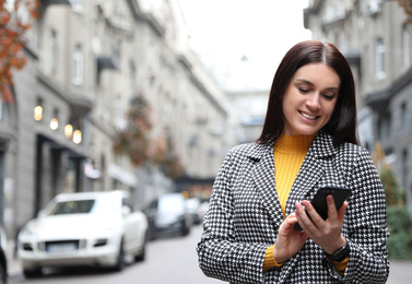 Photo of Beautiful woman in stylish suit using smartphone on city street. Space for text