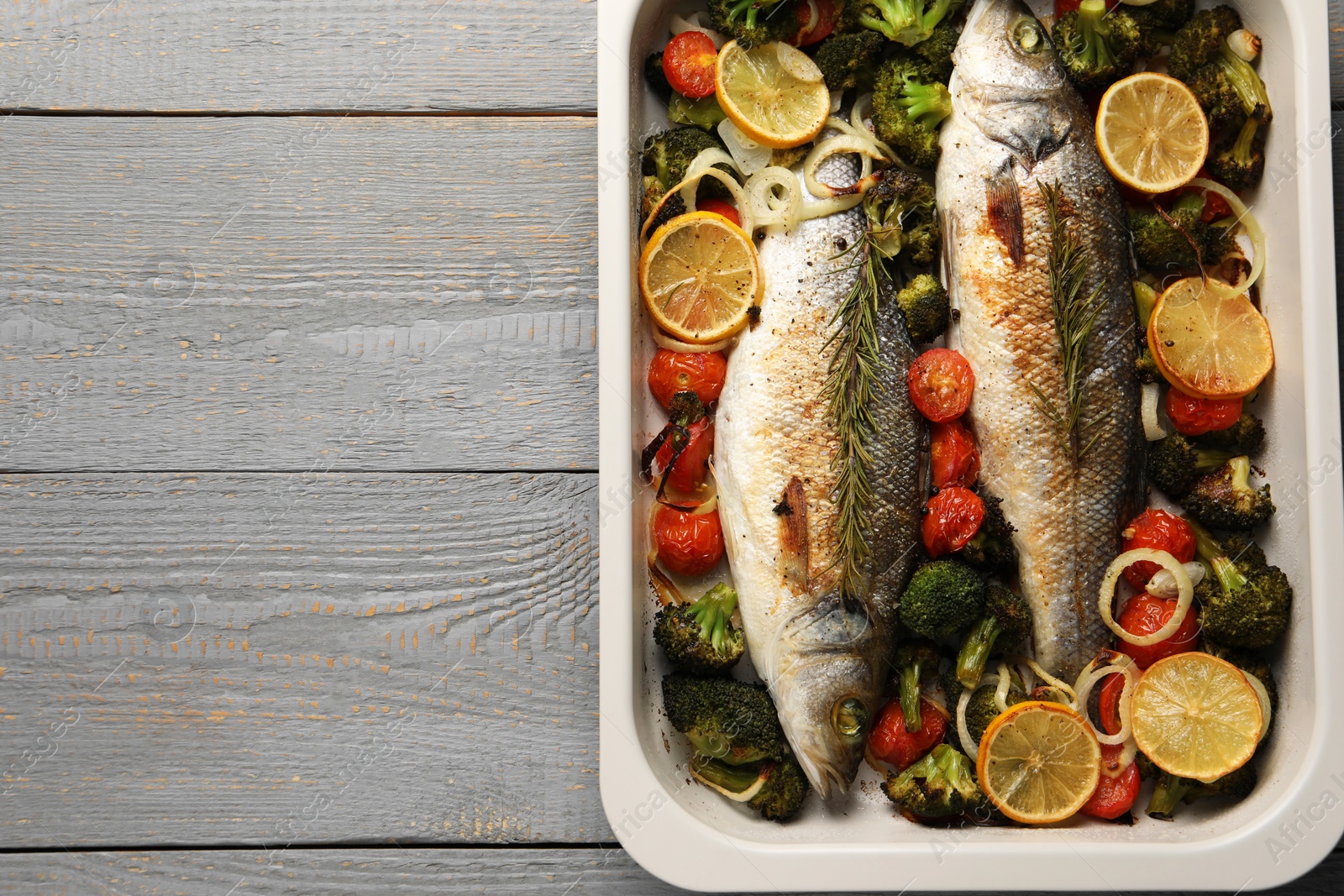 Photo of Delicious fish with vegetables and lemon in baking dish on grey wooden table, top view. Space for text