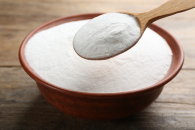 Photo of Baking soda in spoon and bowl on wooden table, closeup