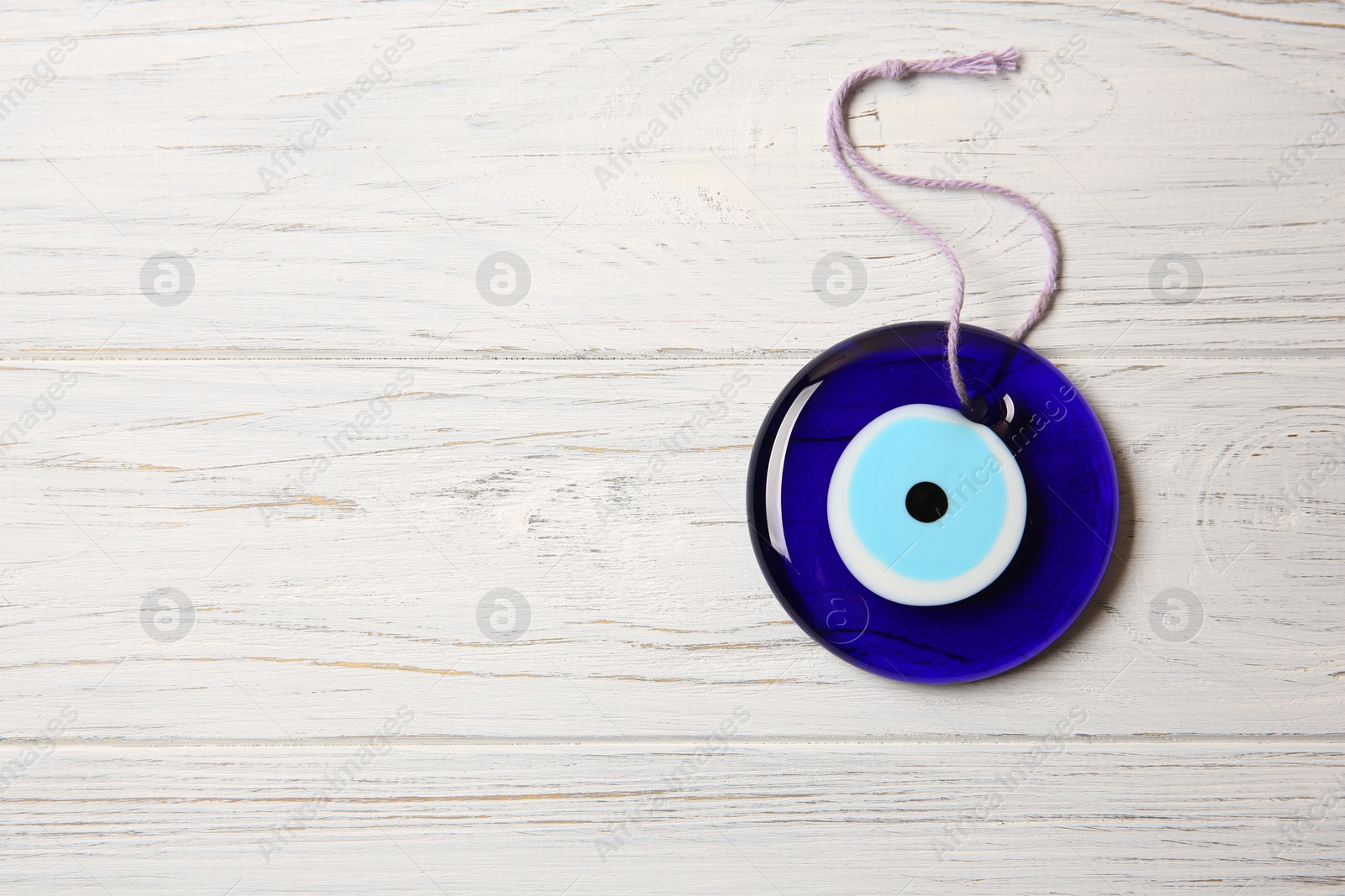 Photo of Evil eye amulet on white wooden table, top view. Space for text