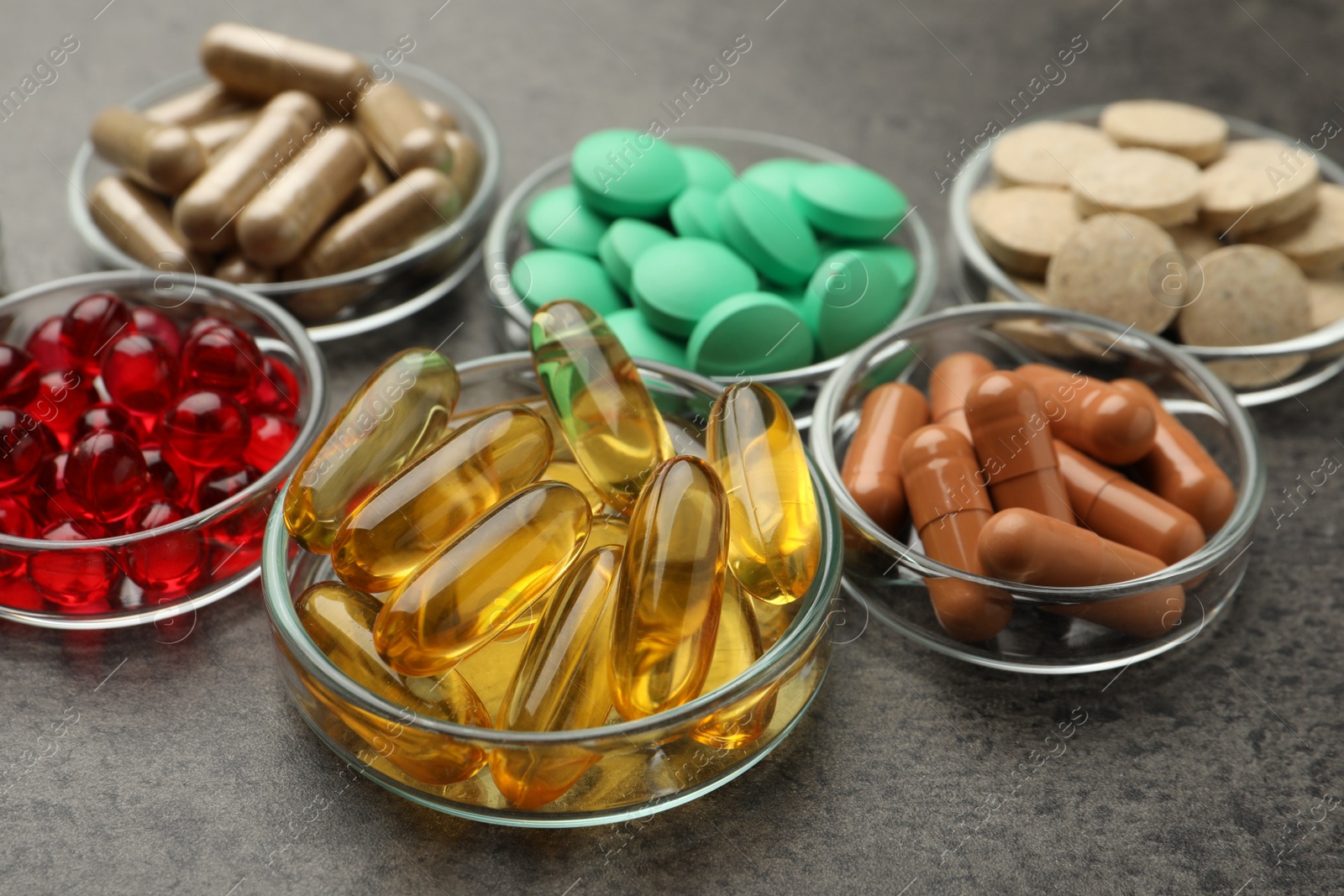 Photo of Different dietary supplements in glass bowls on grey table