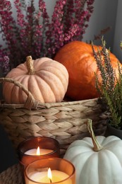 Photo of Wicker basket with beautiful heather flowers, pumpkins and burning candles on table