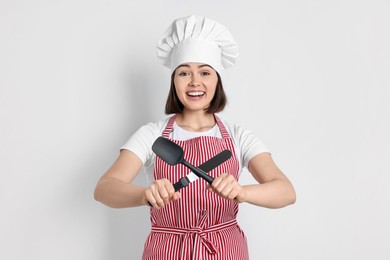 Happy confectioner holding spatulas on light grey background
