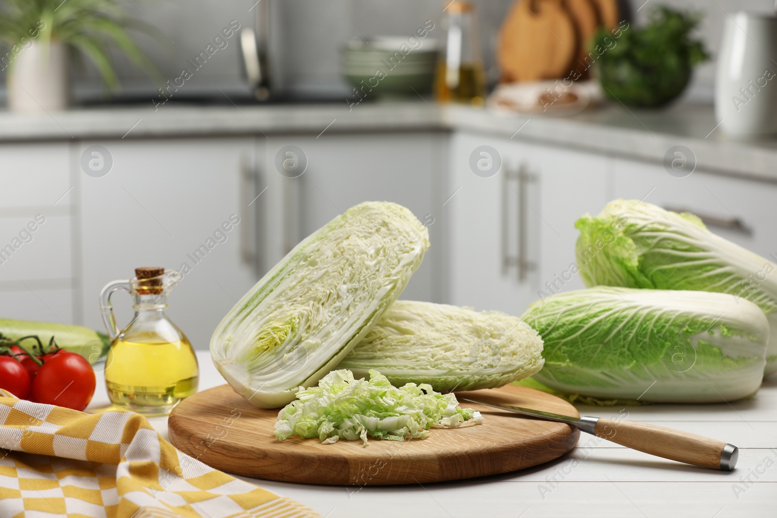 Photo of Fresh Chinese cabbages, knife, tomatoes and oil on white wooden table in kitchen