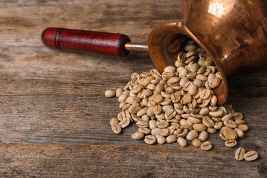 Photo of Overturned jezve with green coffee beans and space for text on wooden background