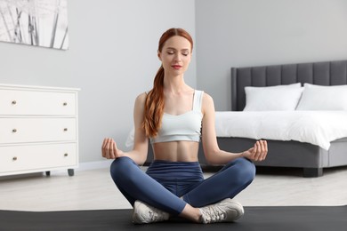 Photo of Young woman in sportswear meditating in bedroom