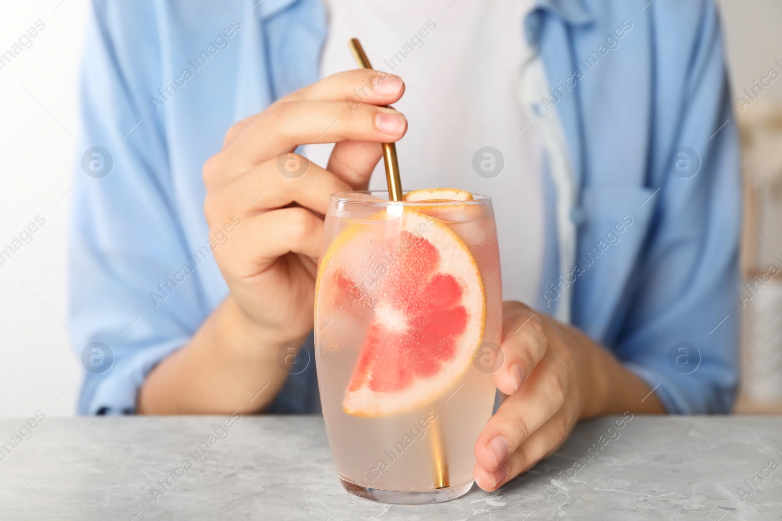 Photo of Woman with glass of grapefruit refreshing drink at grey marble table, closeup