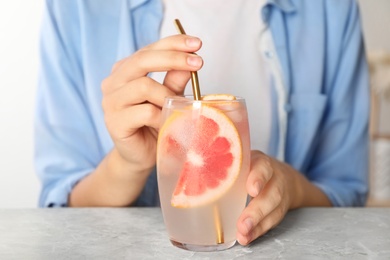 Photo of Woman with glass of grapefruit refreshing drink at grey marble table, closeup