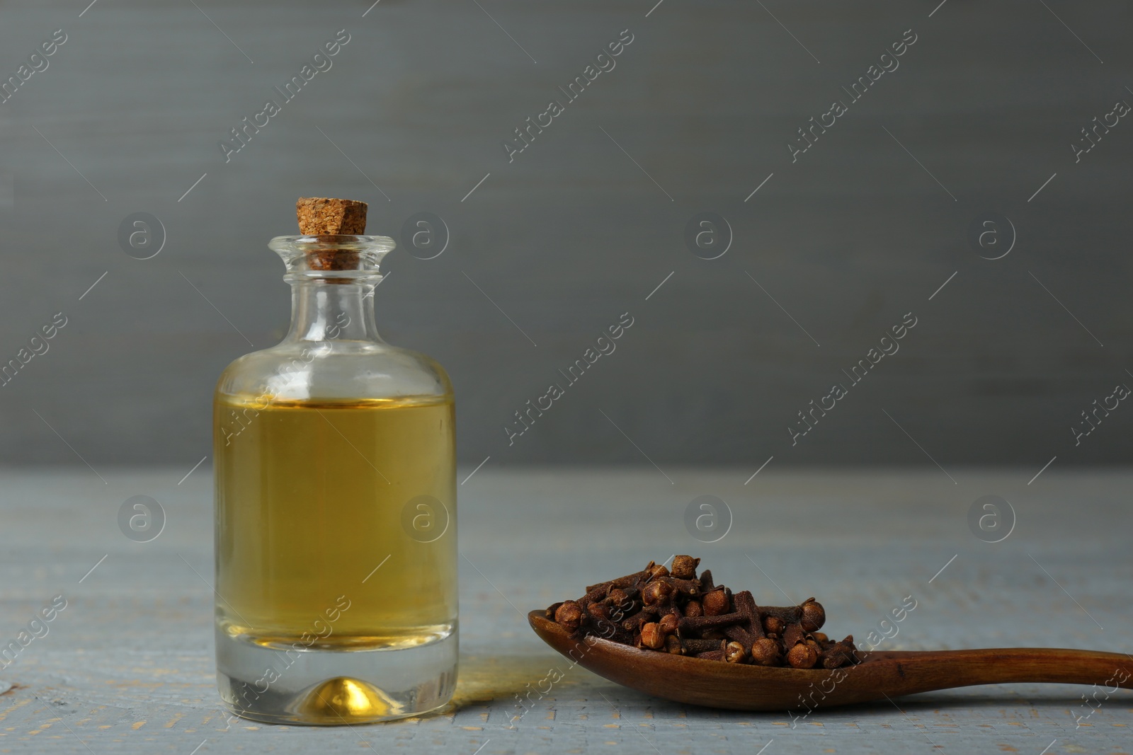 Photo of Essential oil and dried cloves on grey wooden table. Space for text