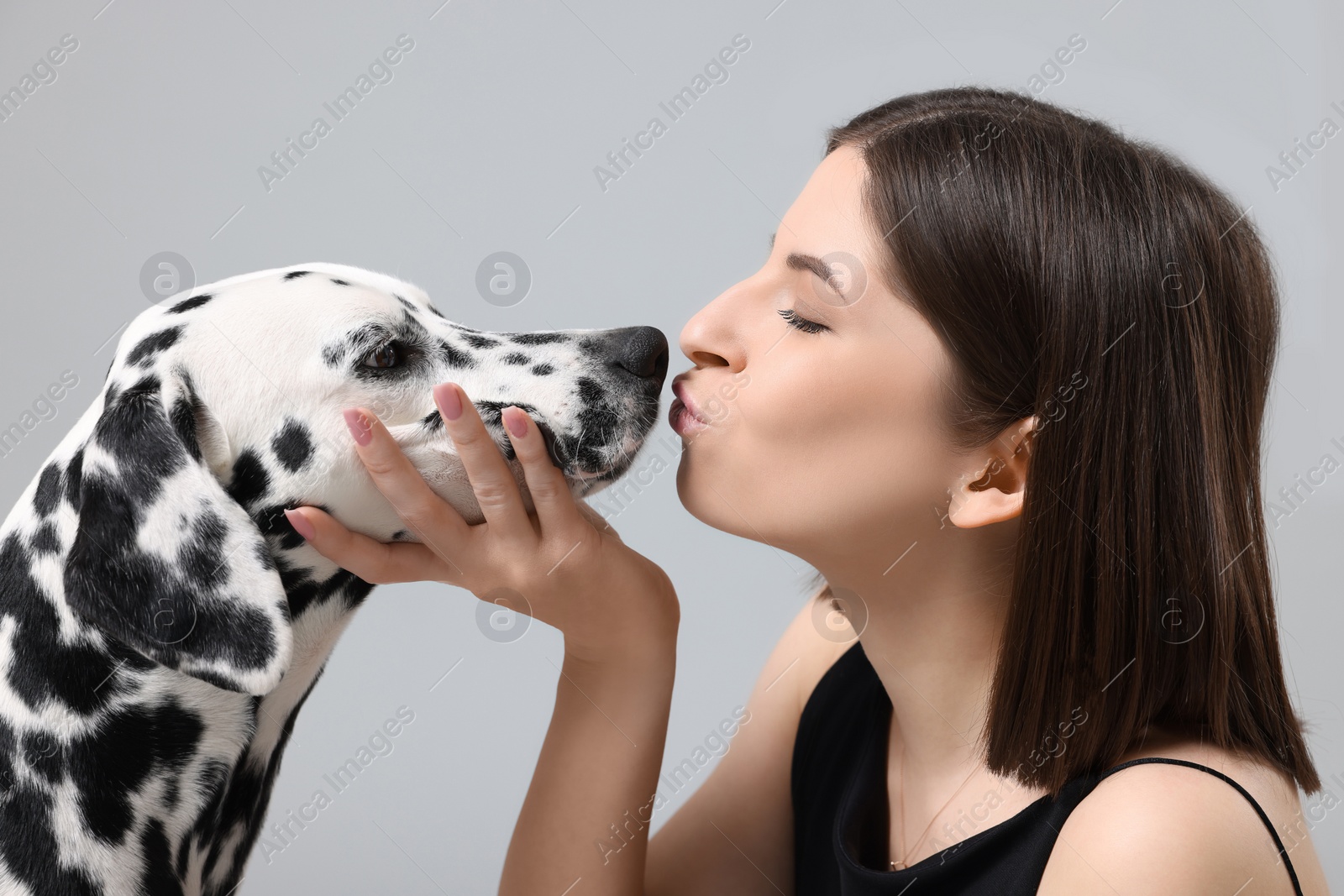 Photo of Beautiful woman kissing her adorable Dalmatian dog on light grey background. Lovely pet