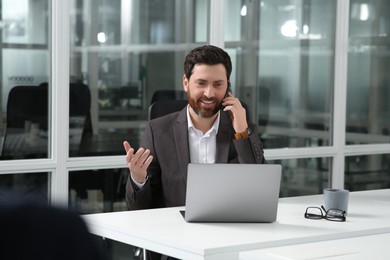 Man talking on phone while working with laptop at white desk in office