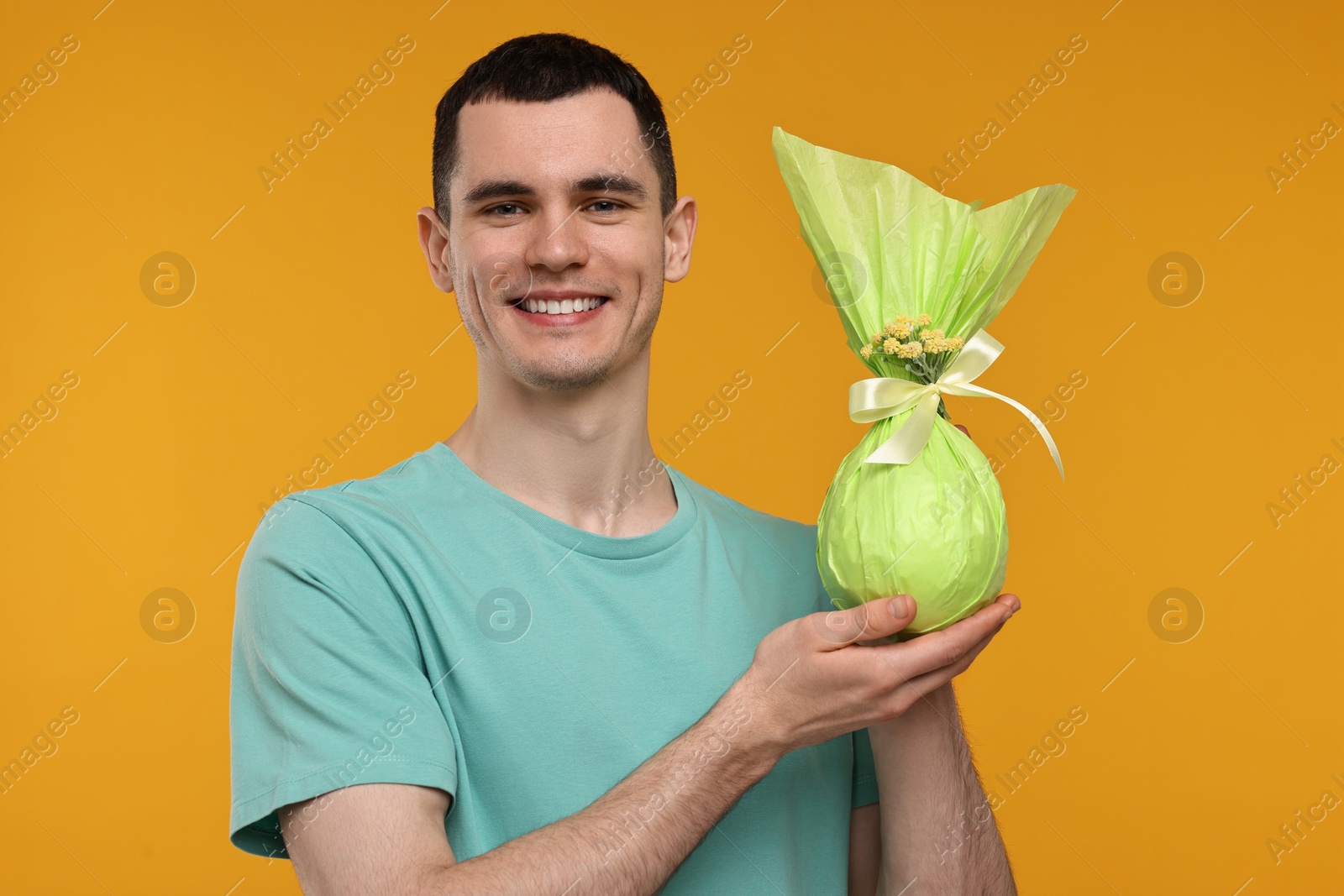 Photo of Easter celebration. Handsome young man with wrapped gift on orange background