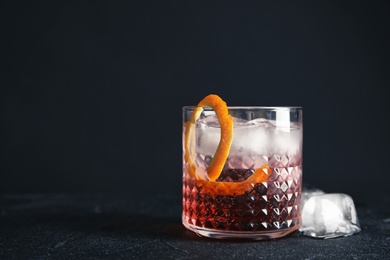 Glass of refreshing cocktail with ice cubes on dark background. Space for text