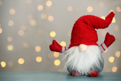 Photo of Cute Christmas gnome on turquoise wooden table against blurred festive lights. Space for text