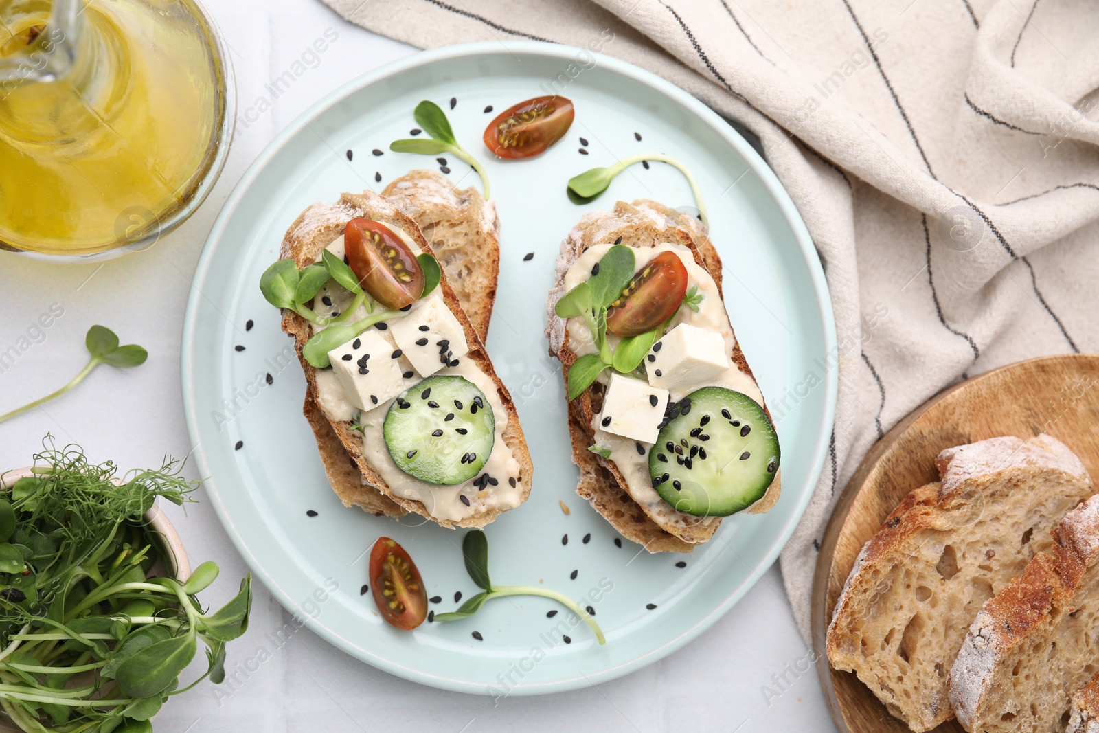 Photo of Tasty vegan sandwiches with tofu, cucumber, tomato and sesame seeds on white tiled table, flat lay