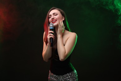 Photo of Emotional woman with microphone singing in color lights on dark background