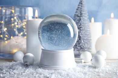 Photo of Magical empty snow globe with Christmas decorations and candles on table