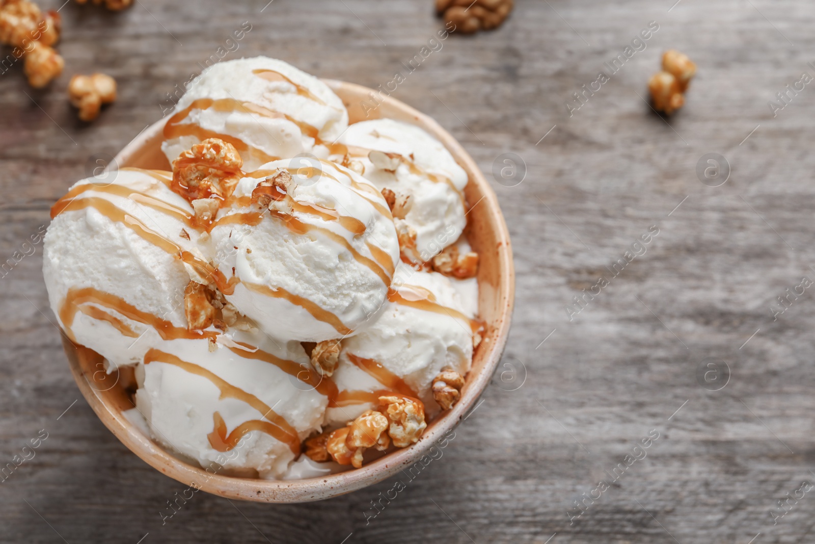 Photo of Tasty ice cream with caramel sauce and popcorn in bowl on wooden table, top view