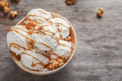 Photo of Tasty ice cream with caramel sauce and popcorn in bowl on wooden table, top view