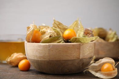 Photo of Ripe physalis fruits with calyxes in bowl on wooden table, closeup