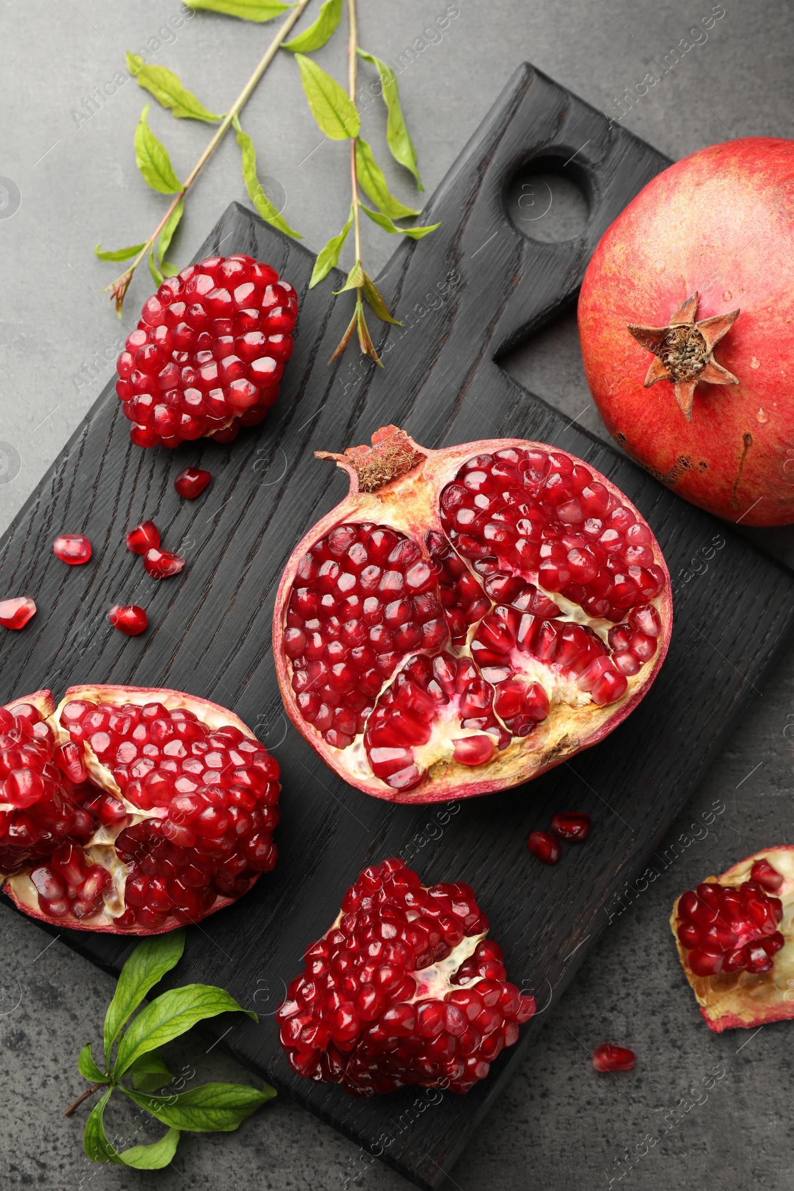 Photo of Fresh pomegranates and green leaves on grey table, top view