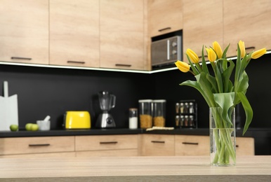 Glass vase with tulips on table in kitchen