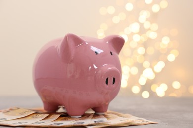 Photo of Piggy bank with euro banknotes on grey table against blurred lights, space for text