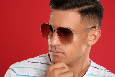 Photo of Handsome man wearing sunglasses on red background, closeup