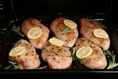 Photo of Chicken breasts with lemon and rosemary on baking sheet in oven