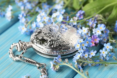 Photo of Beautiful Forget-me-not flowers and pocket watch on light blue wooden table, closeup