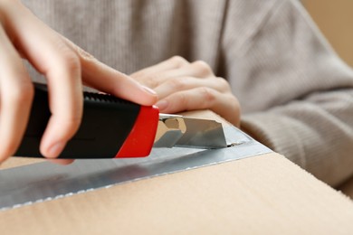 Woman using utility knife to open parcel, closeup