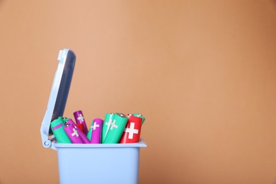 Many used batteries in recycling bin on light brown background. Space for text