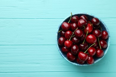 Photo of Fresh ripe cherries in bowl on turquoise wooden table, top view. Space for text